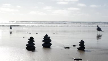 Okyanus sahilinde dengelenen kayalar, deniz dalgalarıyla istiflenen taşlar. Kumlu sahilde çakıl taşı piramidi