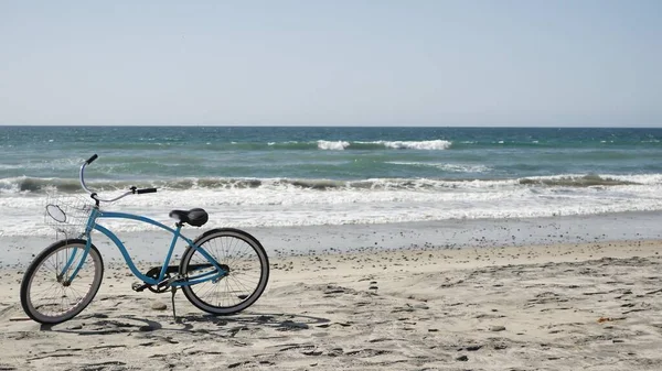 Bicycle cruiser bike by ocean beach California coast USA. Summertime blue cycle, sand and water wave