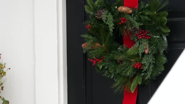 Corona de Navidad verde de pino o abeto y cinta roja en la puerta, decoración de Año Nuevo. — Vídeo de stock