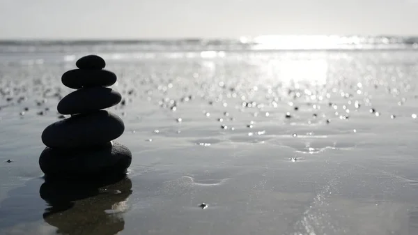 Rock balancing on ocean beach, stones stacking by sea water waves. Pyramid of pebbles on sandy shore