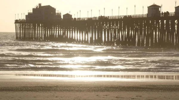 Muelle de madera sobre pilotes, silueta al atardecer, California USA, Oceanside. Olas soleadas al atardecer. — Foto de Stock