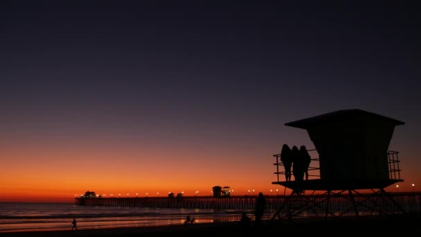 Young teen girls silhouettes, lifeguard watch tower, friends on pacific ocean beach, California USA. — Stock Video