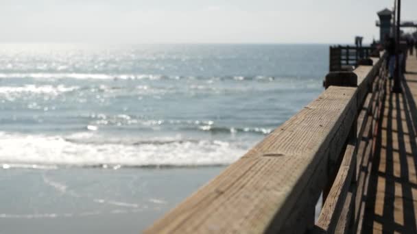 Wooden pier waterfront boardwalk, California beach USA. Defocused ocean, sea waves. People walking. — Stock Video