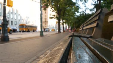 New York 'taki Central Park yakınlarında ahşap bank, Birleşik Devletler. Arabalar ve insanlar Manhattan, ABD 'de sokakta. Odaklanmamış perspektif. Sarı okul otobüsü yolda..
