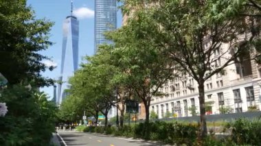 Aşağı Manhattan Finansal Bölgesi, New York, ABD. Bir Dünya Ticaret Merkezi gökdelen binası, Battery Park 'tan Özgürlük Kulesi. Yaz ağaçları yeşillik, Batı sokağı perspektifi.