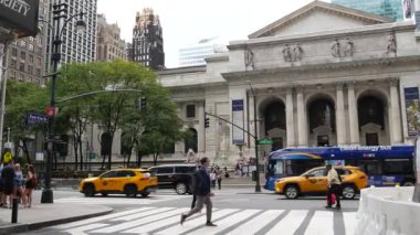 New York, ABD - 10 Eylül 2024: 5. Cadde, Manhattan Midtown Caddesi. Zebra kavşağından geçen yayalar, yoldan geçen sarı taksi. Halk kütüphanesi mimarisi.