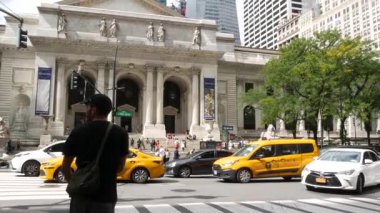 New York, ABD - 10 Eylül 2024: 5. Cadde, Manhattan Midtown Caddesi. Zebra kavşağından geçen yayalar, yoldan geçen sarı taksi. Halk kütüphanesi mimarisi.