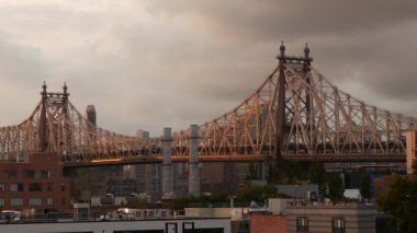 Queens, Queensboro Köprüsü mimarisinden New York City Manhattan şehir merkezi silueti. Çatıdan şehir manzarası, Long Island Hunters Point. Ulaşım köprüsünün üzerinde gün batımı. Yağmurlu bulutlar.