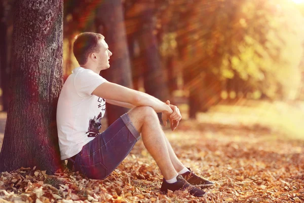 Молодой человек сидит в осеннем парке — стоковое фото