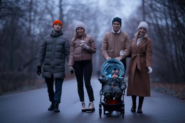 Grup arkadaşları yetişkinler kasvetli sonbaharı park eder, genç ebeveynler şehirde gezer Kasım ayında.