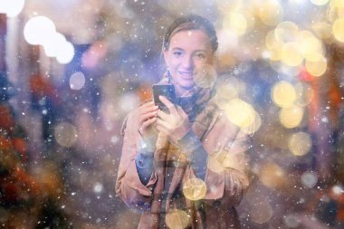 Mutlu kız akşam alışverişi yapıyor. Dükkanın penceresinin yanında duruyor.