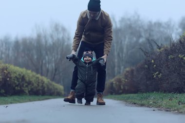 İlk adım çocuk yürümeyi öğrenir, çocuk ve babası sonbaharda parkta yürür, kış tarzında Kasım ayında.