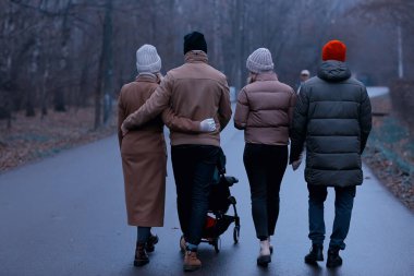 Grup arkadaşları yetişkinler kasvetli sonbaharı park eder, genç ebeveynler şehirde gezer Kasım ayında.