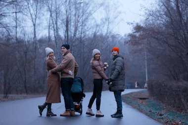 Grup arkadaşları yetişkinler kasvetli sonbaharı park eder, genç ebeveynler şehirde gezer Kasım ayında.