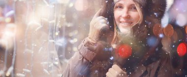 Mutlu kız akşam alışverişi yapıyor. Dükkanın penceresinin yanında duruyor.