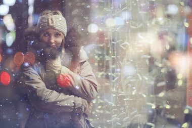 Mutlu kız akşam alışverişi yapıyor. Dükkanın penceresinin yanında duruyor.