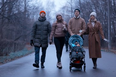 Grup arkadaşları yetişkinler kasvetli sonbaharı park eder, genç ebeveynler şehirde gezer Kasım ayında.
