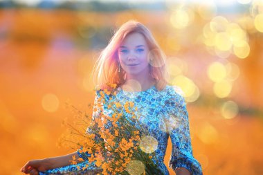 Çiçeklerle dolu güneşli bir tarlada yaz kızı, doğada sıcak, mutlu bir gün batımı