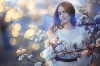 Yetişkin mutlu bir kadının bahar portresi çiçek açan bir bahçede, güneş ışınları ve parıltı, Nisan çiçekli kız