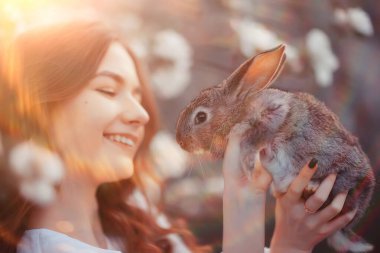 Paskalya tavşanı güzel bir kızın elinde, bahar, nisan, çiçek açan bir bahçede, bir kadın portresi