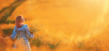 Çiçeklerle dolu güneşli bir tarlada yaz kızı, doğada sıcak, mutlu bir gün batımı