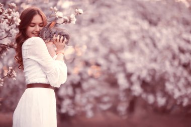 Paskalya tavşanı güzel bir kızın elinde, bahar, nisan, çiçek açan bir bahçede, bir kadın portresi