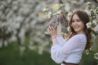 Paskalya tavşanı güzel bir kızın elinde, bahar, nisan, çiçek açan bir bahçede, bir kadın portresi