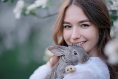 Paskalya tavşanı güzel bir kızın elinde, bahar, nisan, çiçek açan bir bahçede, bir kadın portresi