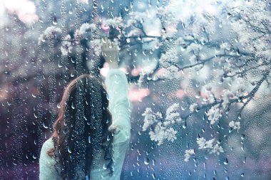 Genç kız baharda çiçek açan bir bahçede portre, baharda mutluluk, nisan ayında yağmur havası