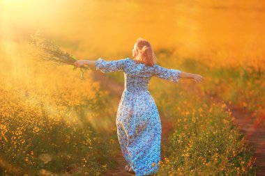 Bahar doğası. Çiçek tarlasında genç bir kız. Güneşli bir manzarada bir bayanın özgürlüğü ve mutluluğu.