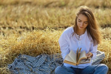 Yazın tarlada kitap okuyan bir kadın bir kitap okuyor. Bir kitap okuyor. Okul kızından yaz tatilini tarlada okuyor.