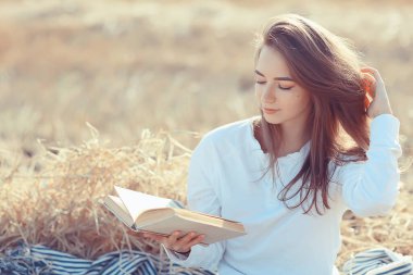 Yazın tarlada kitap okuyan bir kadın bir kitap okuyor. Bir kitap okuyor. Okul kızından yaz tatilini tarlada okuyor.