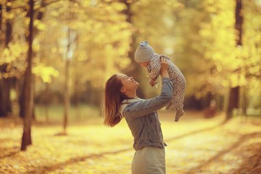 Anne bebeği sonbahar parkına fırlatıyor, mutluluk sarı doğa düşüyor.