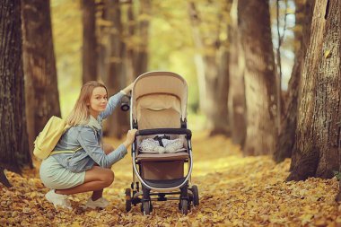 Annem sonbahar parkında yürüyüş için bebek arabasıyla gezer, sonbahar manzarası Ekim ayı sarı park manzarası