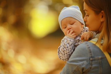 Anne bebeğini kucağında tutuyor, sonbahar parkında, açık havada aile geçmişi.
