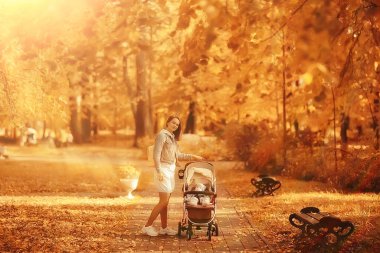 Annem sonbahar parkında yürüyüş için bebek arabasıyla gezer, sonbahar manzarası Ekim ayı sarı park manzarası