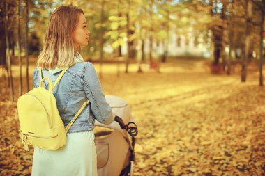 Annem sonbahar parkında yürüyüş için bebek arabasıyla gezer, sonbahar manzarası Ekim ayı sarı park manzarası