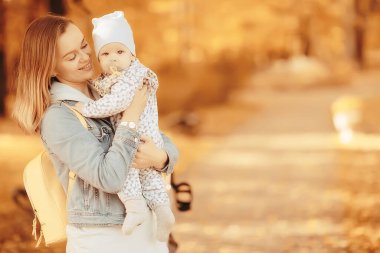 Anne bebeğini kucağında tutuyor, sonbahar parkında, açık havada aile geçmişi.