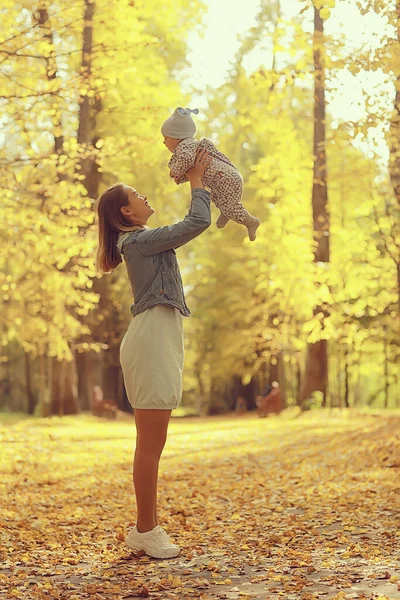 妈妈把孩子扔到了秋天的公园里 快乐的黄自然落下了 — 图库照片