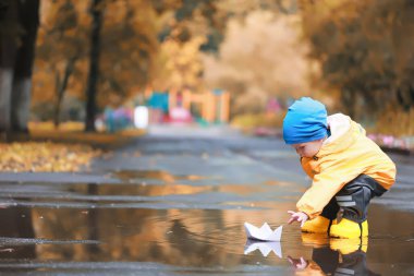 Kağıt tekne su birikintisi oyunu, erkek sezonu sonbahar yağmurluğu, sarı lastik çizmeler, açık hava oyunu