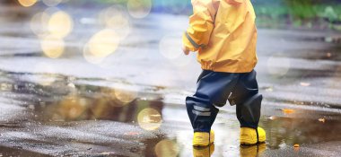 Su birikintilerinde dışarıda oynayan çocuk, sonbahar çocukluğunda lastik ayakkabılar, sarı yağmurluklar.