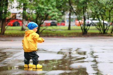 Su birikintilerinde dışarıda oynayan çocuk, sonbahar çocukluğunda lastik ayakkabılar, sarı yağmurluklar.