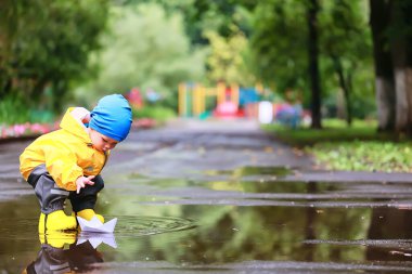 Kağıt tekne su birikintisi oyunu, erkek sezonu sonbahar yağmurluğu, sarı lastik çizmeler, açık hava oyunu