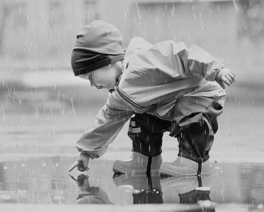 Su birikintilerinde dışarıda oynayan çocuk, sonbahar çocukluğunda lastik ayakkabılar, sarı yağmurluklar.