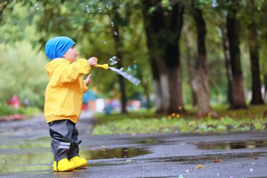 Parkta sonbahar, küçük çocuk yağmurlukla yürüyor mevsimlik görünüş