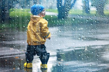 Yağmur yürüyüşü çocuk, sonbaharda parkta yağmur damlaları ve su birikintileri çocuk