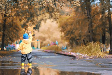 Su birikintilerinde dışarıda oynayan çocuk, sonbahar çocukluğunda lastik ayakkabılar, sarı yağmurluklar.