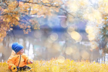 Sarı yağmurluklu çocuk, bak, sonbahar mevsimi parkta yürüyor.