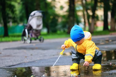 Su birikintilerinde dışarıda oynayan çocuk, sonbahar çocukluğunda lastik ayakkabılar, sarı yağmurluklar.