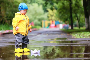 Su birikintilerinde dışarıda oynayan çocuk, sonbahar çocukluğunda lastik ayakkabılar, sarı yağmurluklar.